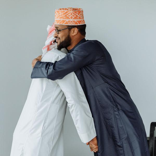 Man wearing white collared thobe being congratulated for his nikah by another man wearing charcoal collared thobe and kufi