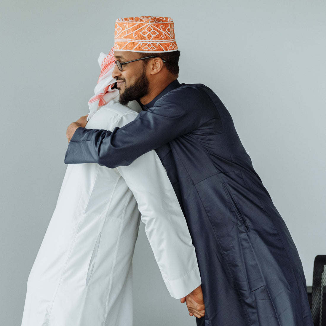 Man wearing white collared thobe being congratulated for his nikah by another man wearing charcoal collared thobe and kufi