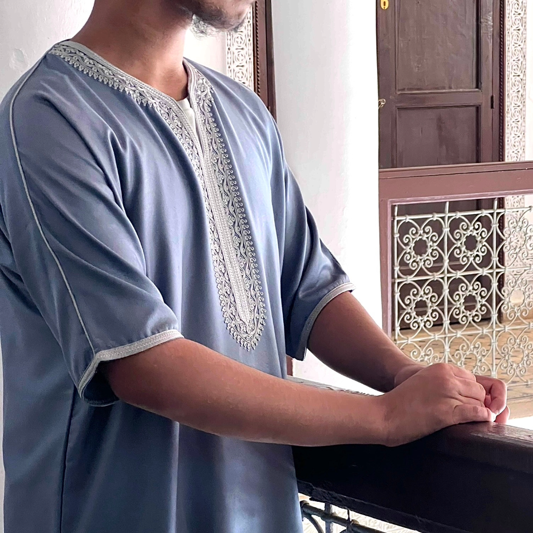 Men's Moroccan gandoura in blue with embroidered neckline worn indoors in a traditional setting