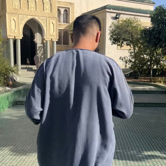 Man blue wearing a navy Moroccan gandoura walking into a mosque courtyard in Fes Morocco
