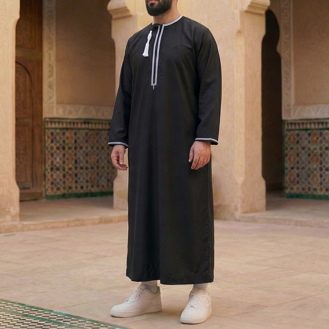 man wearing black omani thobe with with white embroidery and detachable tassel