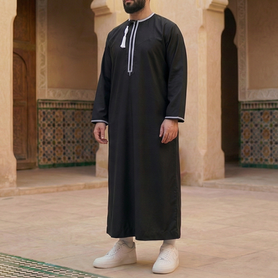 man wearing black omani thobe with with white embroidery and detachable tassel